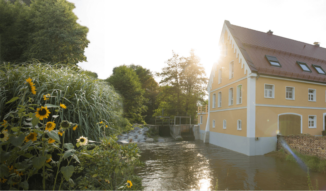 Haus am Rand eines Flusses, mit Sonnenuntergang und Sonnenblumen